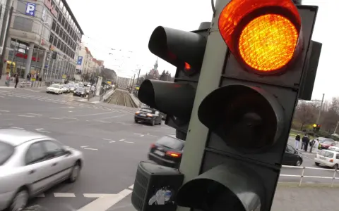 Żółte światło na sygnalizatorze drogowym, ruch uliczny i budynki w tle.