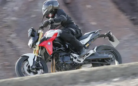 Motocyklista w kasku i kombinezonie pędzi na motocyklu BMW F900R po kamienistym terenie.