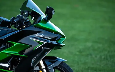 Błyszczący, czarno-zielony motocykl Kawasaki H2 SX z napisem "Ninja H2 SX" na owiewce, zaparkowany na tle zielonej trawy.