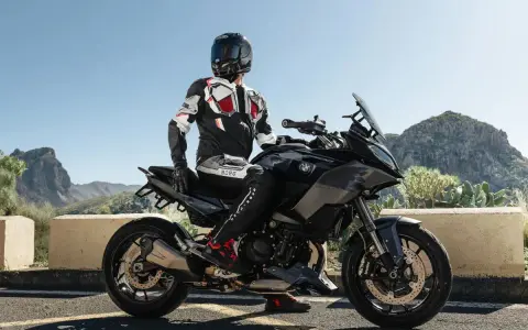 Motocyklista w kombinezonie na czarnym motocyklu BMW, gotowy do podróży po górskich drogach. Wśród wielu marek motocykli, ta prezentuje się imponująco.
