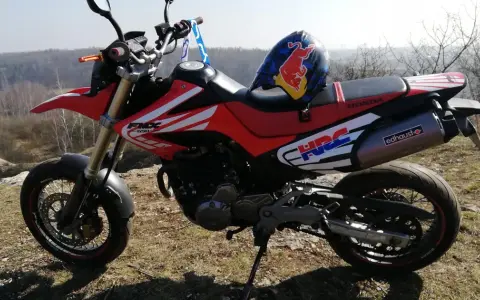 Czerwony motocykl Honda FMX 650 z kaskiem Red Bull na siedzeniu, gotowy na przygodę w terenie.
