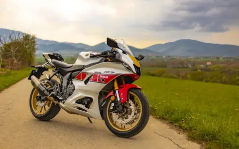 Sportowy motocykl Yamaha R7 w białym malowaniu z czerwonymi akcentami, zaparkowany na drodze wśród zielonych wzgórz. Sprawdź aktualną yamaha r7 cena!