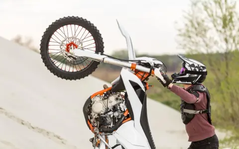 Motocyklista w kasku i ochraniaczach wykonuje wheelie na piaskowej wydmie. To najszybszy cross na świecie, gotowy do akcji.