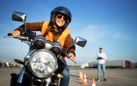 Uśmiechnięta kursantka w kamizelce odblaskowej i kasku na motocyklu, przygotowuje się do egzaminu na prawo jazdy A2.