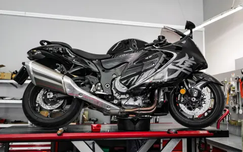 Czarny motocykl na podnośniku, gotowy do serwisu. Widać duży, chromowany wydech, który odcina się od reszty maszyny.