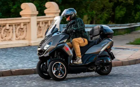 Mężczyzna w kasku jedzie trójkołowym skuterem Peugeot Metropolis 400. Widoczna jest jego prędkość maksymalna.