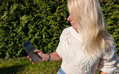 Blondynka w białym swetrze korzysta z telefonu, by wyznaczyć trasę krok po kroku.