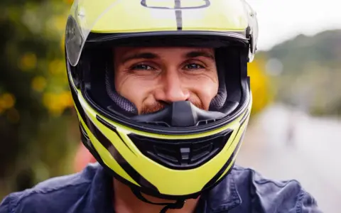 Uśmiechnięty mężczyzna w żółtym kasku motocyklowym.