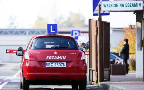 Czerwony samochód z literą "L" na dachu i napisem "EGZAMIN" czeka przed bramą. Czy trudno zdać prawo jazdy?