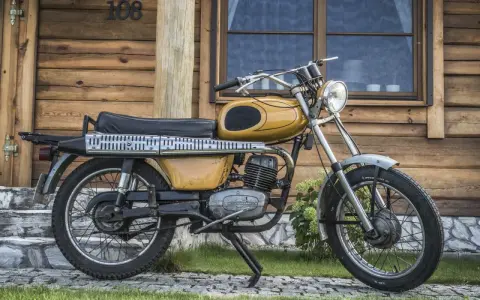 Żółty motorower WSK 175, z widocznymi danymi technicznymi na silniku, stoi przed drewnianym domem.