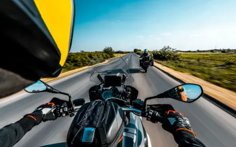Przełęcz Salmopolska widziana z perspektywy motocyklisty. Droga wijąca się pośród zielonych pól, błękitne niebo i inny motocykl przed nami.