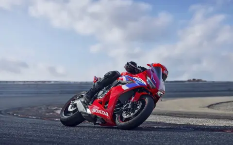 Czerwony motocykl Honda CBR650R z kierowcą pochylonym na zakręcie toru wyścigowego.