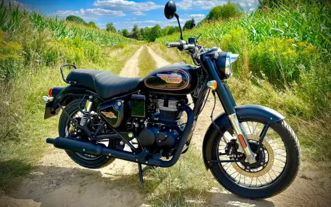 Czarny motocykl Royal Enfield Diesel na polnej drodze, otoczony zielenią i kukurydzą.