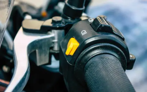 Pomarańczowy przycisk na kierownicy motocykla, który może służyć jako kill switch, obok przełącznika świateł.