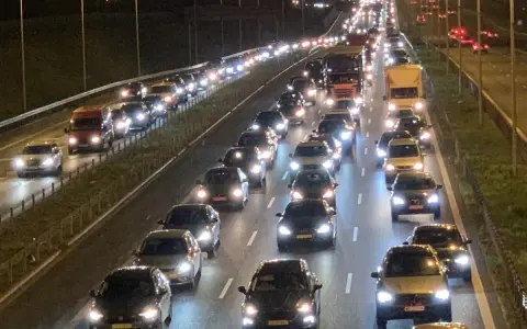 Nocny korek na drodze S8. Długi sznur samochodów i ciężarówek z zapalonymi światłami tworzy świetlisty tunel.