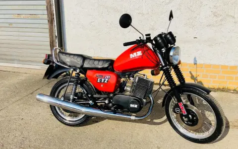 Czerwony motocykl MZ ETZ 251 z lat 80. stoi przed garażem.