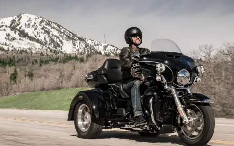 Mężczyzna w kasku i skórzanej kurtce jedzie czarnym motocyklem trójkołowym L5E. W tle góry ze śniegiem.