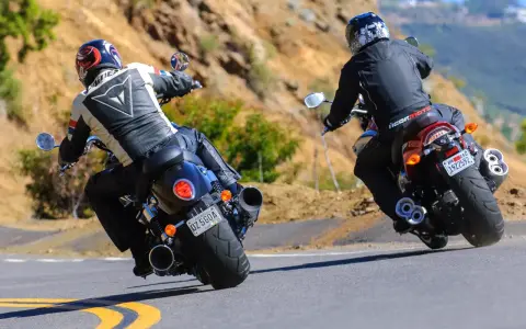 Dwóch motocyklistów na zakręcie. Jeden na Yamaha R3, drugi na V-Max, w skórzanych kombinezonach, pokonuje górską drogę.