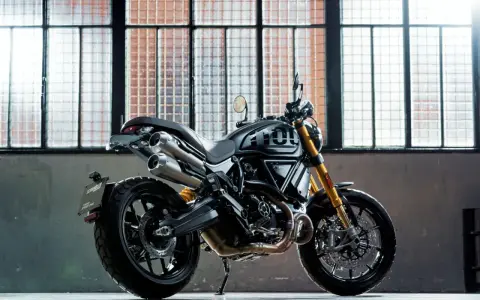 Czarny motor scrambler z podwójnym wydechem i złotym zawieszeniem, gotowy do jazdy po miejskich ulicach.