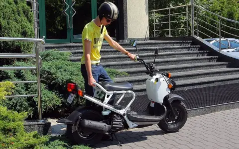 Młody mężczyzna w kasku i żółtej koszulce przy białym skuterze. To jego stara karta motorowerowa, gotowa do jazdy.