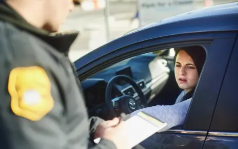 Policjant wręcza kobiecie w samochodzie mandaty w Austrii. Kobieta wygląda na zmartwioną.