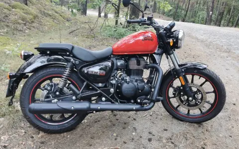 Czerwony Royal Enfield Meteor 350 na leśnej drodze. Klasyczny wygląd i gotowość do podróży.