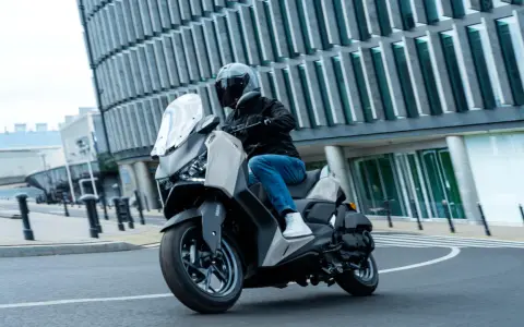 Mężczyzna w kasku jedzie skuterem Yamaha X-MAX 125 po mieście. Czy to lepszy wybór niż Honda Forza 125?