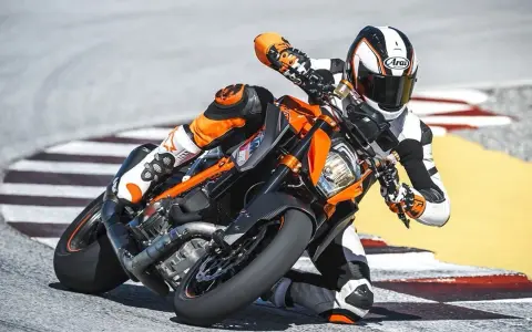 Motocyklista w kombinezonie ściga się na torze na pomarańczowym KTM 1290 Super Duke, pochylony w zakręcie.