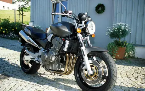 Szary motocykl Honda 919 zaparkowany na bruku przed domem.
