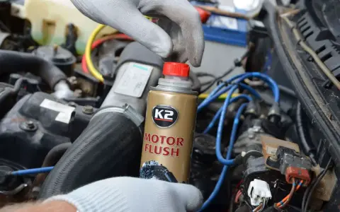Ręka w rękawiczce trzyma puszkę płukanki do silnika motocyklowego K2 Motor Flush, gotowa do użycia w silniku.