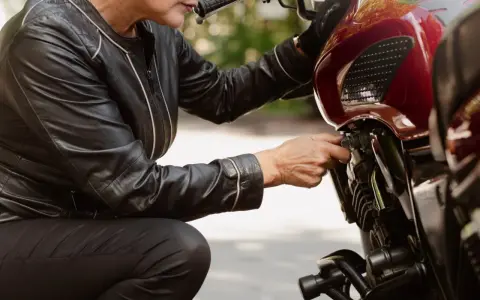 Kobieta w skórzanej kurtce sprawdza regulator napięcia w motocyklu.