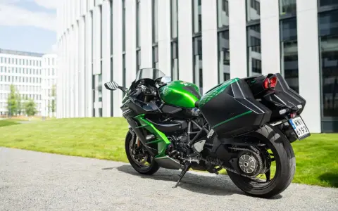 Zielony Kawasaki Ninja H2 z czarnymi kuframi, gotowy do podróży obok nowoczesnego budynku.