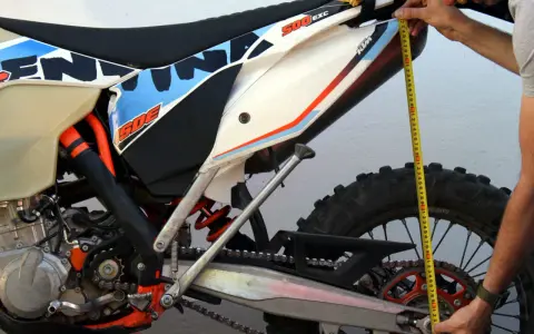 Mierzenie preload w amortyzatorze motocykla KTM 500 EXC. Dłoń trzyma miarkę przy tylnym kole.