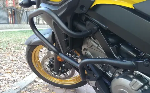 Żółty motocykl z czarnymi gmolami chroniącymi silnik i osłony. Złota obręcz koła i tarcza hamulcowa.