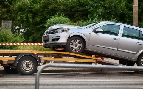 Srebrny samochód po wypadku, bez prawa rejestracji, ładowany na lawetę.
