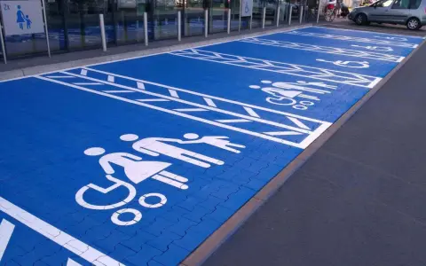 Niebieski parking z białymi symbolami osób na wózkach inwalidzkich i rodzin. Znak P19 informuje o przeznaczeniu miejsc.