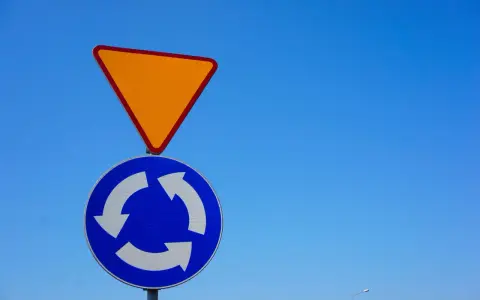 Znak podporządkowania (ustąp pierwszeństwa) i znak ronda na tle błękitnego nieba.