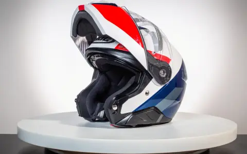 Kask motocyklowy z podniesioną szczęką, w kolorach białym, czerwonym i niebieskim, na białym tle.