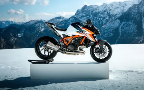 Pomarańczowo-biały KTM Super Duke na śnieżnym tle z górami w tle.