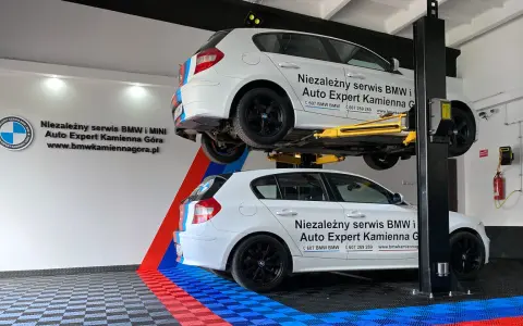 Dwa białe BMW, jedno na podnośniku, w serwisie Auto Expert. W tle logo BMW.