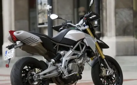 Srebrno-czarny motocykl Aprilia Dorsoduro 750 z żółtymi amortyzatorami, gotowy do jazdy po miejskich ulicach.