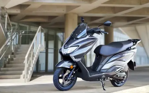 Szary skuter Suzuki Burgman 125 na tle nowoczesnego budynku z betonowymi schodami.