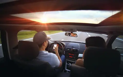 Kierowca z telefonem w ręku, pasażerka obok. Zasada ograniczonego zaufania w praktyce, bo kto wie, co na ekranie?