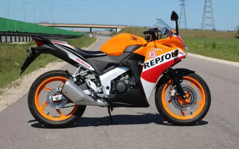 Pomarańczowy motocykl Honda CBR 125 Repsol na drodze. Warto sprawdzić honda cbr 125 dane techniczne przed zakupem.