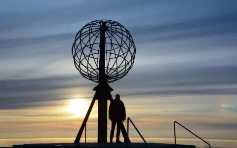 Sylwetka człowieka przy globusie na Nordkapp podczas zachodu słońca.