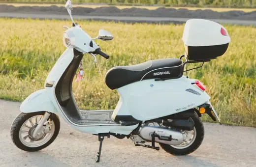 Jasny skuter Mondial Wing 50i, idealny na pierwsze przejażdżki bez prawa jazdy, stoi na tle zielonego pola.