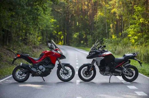 Dwa motocykle Ducati Multistrada, czerwony i czarno-biały, stoją na leśnej drodze.