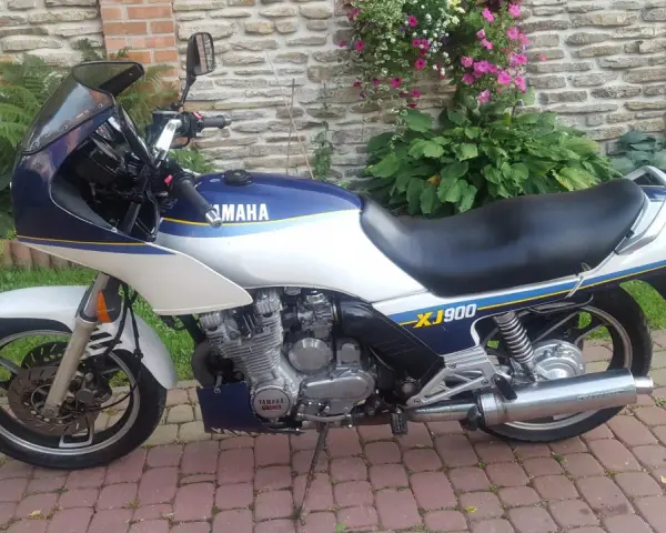 Klasyczny motocykl Yamaha XJ 900 w kolorze białym i granatowym, z niebieskimi i żółtymi pasami, zaparkowany na brukowanym podjeździe.