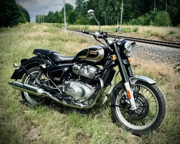 Czarny Royal Enfield Classic 650 lśni chromem na tle torów kolejowych i zieleni. Gotowy na przygodę.