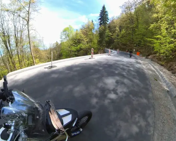 Motocyklista pokonuje zakręty na malowniczej drodze stu zakrętów, otoczonej zielonymi lasami.